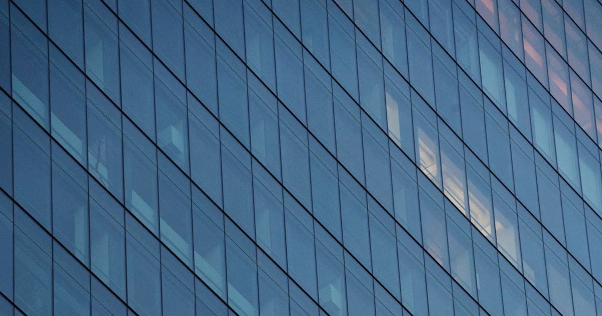 The glass curtain wall of a San Francisco office tower, lit windows visible through the grid of panes