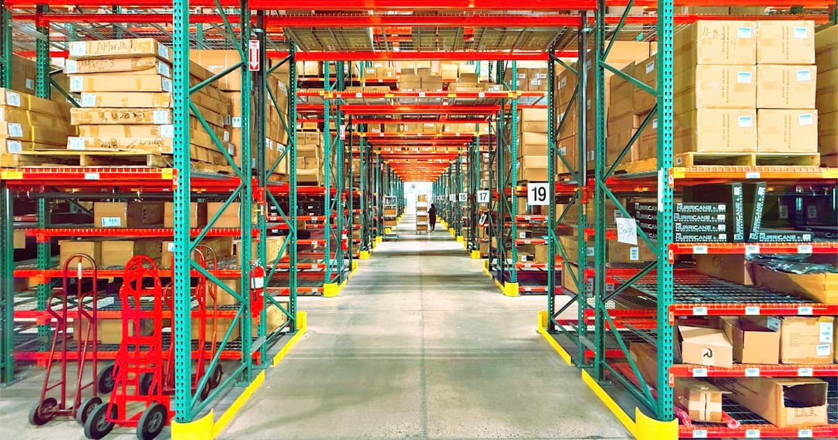 A long aisle between tall steel racks of palletized inventory in a distribution warehouse