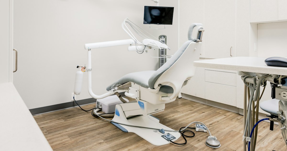 An empty dental operatory with a reclined treatment chair, overhead light arm, and instrument tray