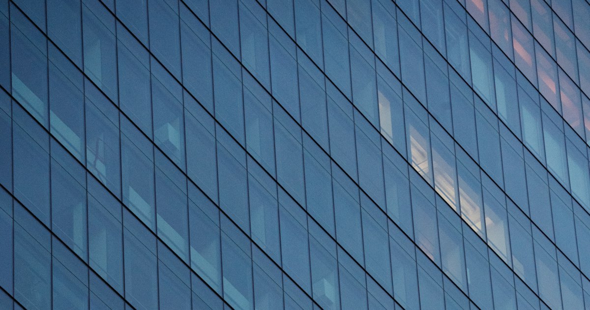 The glass curtain wall of a San Francisco office tower, lit windows visible through the grid of panes