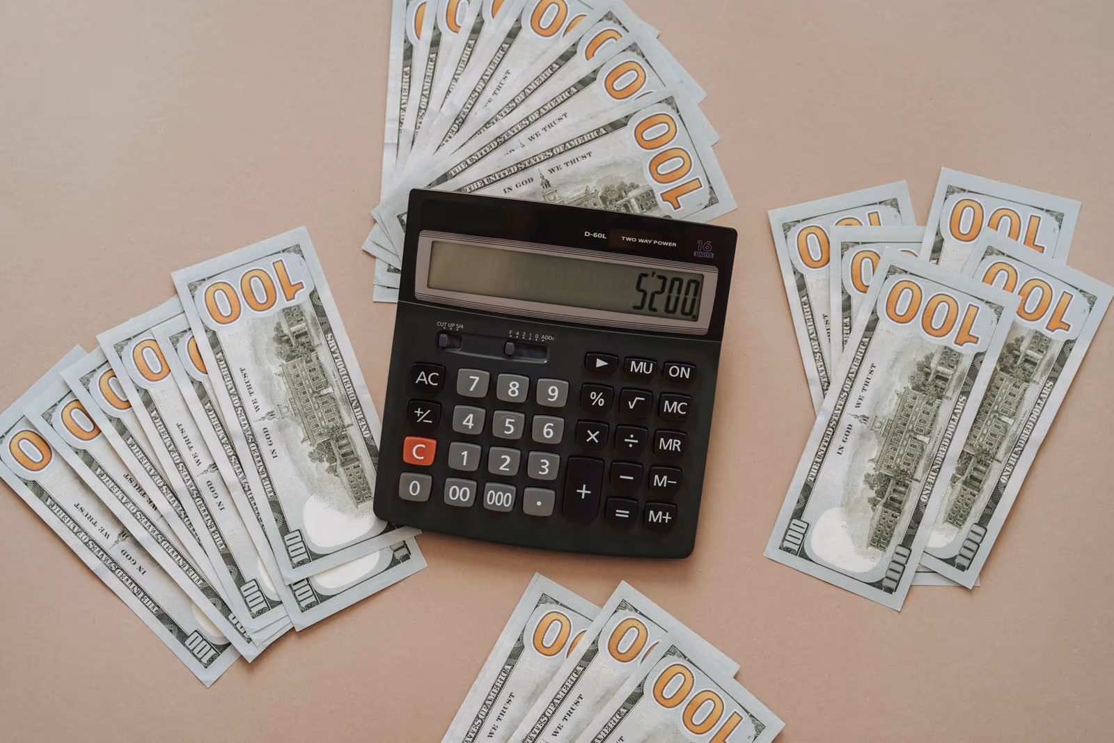 A calculator resting on a fan of U.S. hundred-dollar bills, illustrating the cost of setting up a Cook Islands Trust