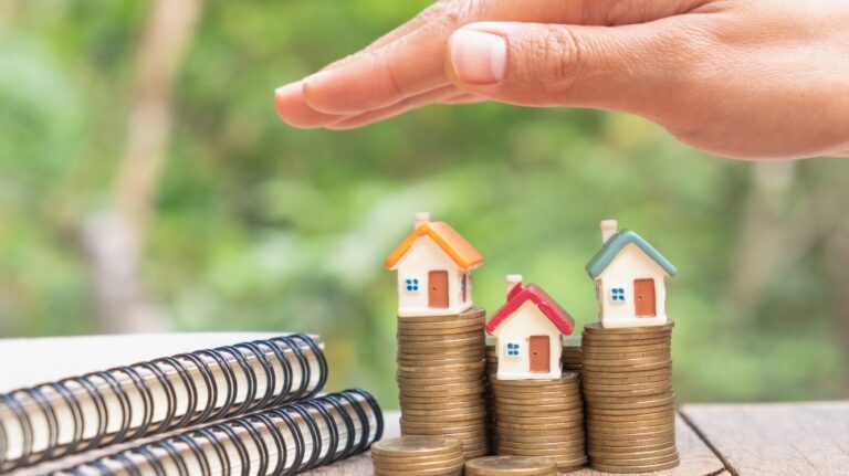 hand covering houses on stack of coins