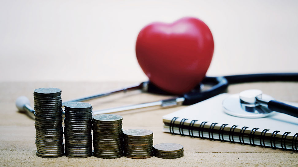 stack of coins notebook stethoscope and heart in wooden table