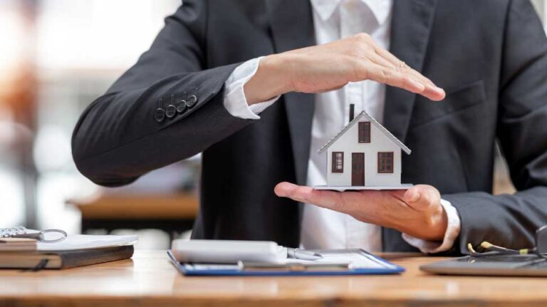 Person in a suit holding a model house with both hands