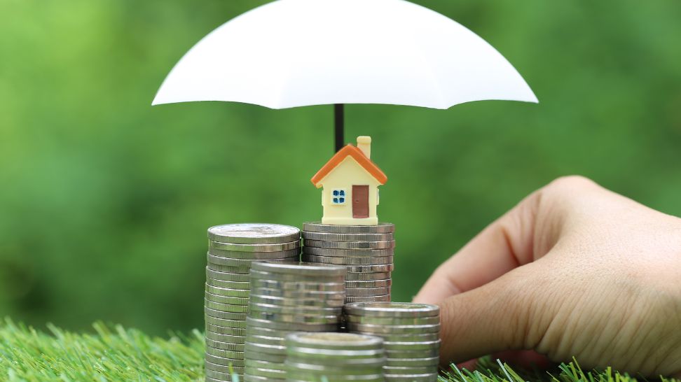 white umbrella covering stack of coins with house model on top