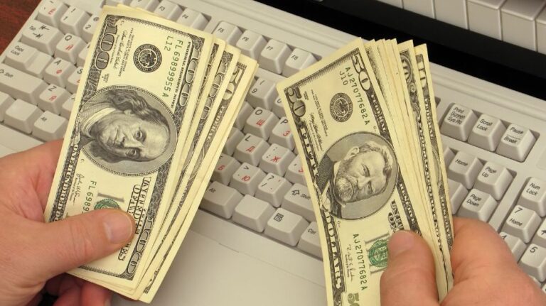 man counting dollar in front of keyboard