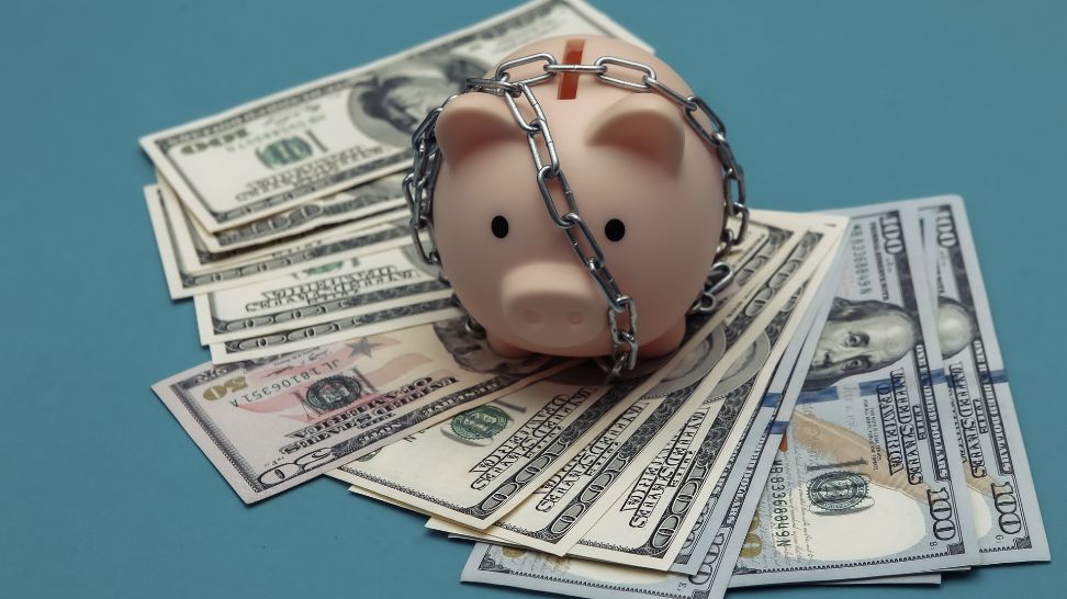 chained piggy bank on pile of US dollar banknotes