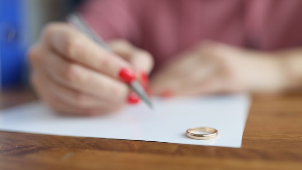 woman writes declaration of divorce with wedding ring resting on the table