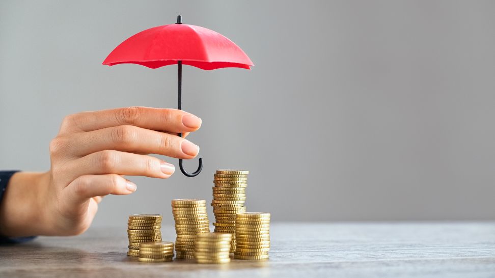hand holding red umbrella covering stack of gold coins