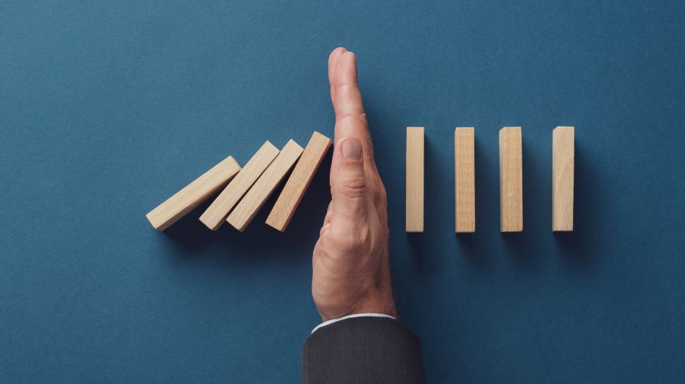 businessman stopping falling dominos from collapsing